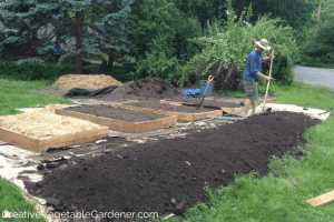 man raking soil in flower garden bed